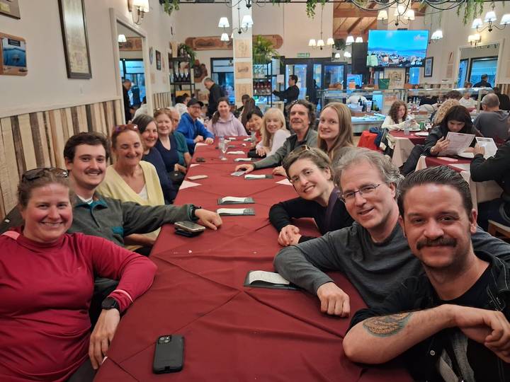 Large tour group gathered around a long restaurant table enjoying a meal together.