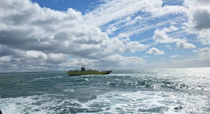Yellow car-ferry crossing choppy teal waters beneath a sky filled with dramatic cloud patterns.