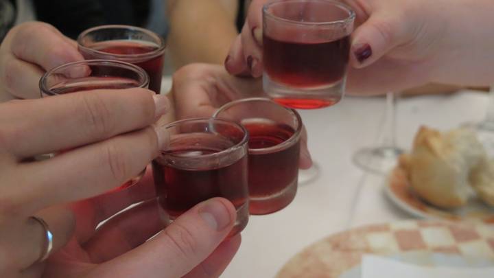 People raising glasses with a reddish drink in a toast.