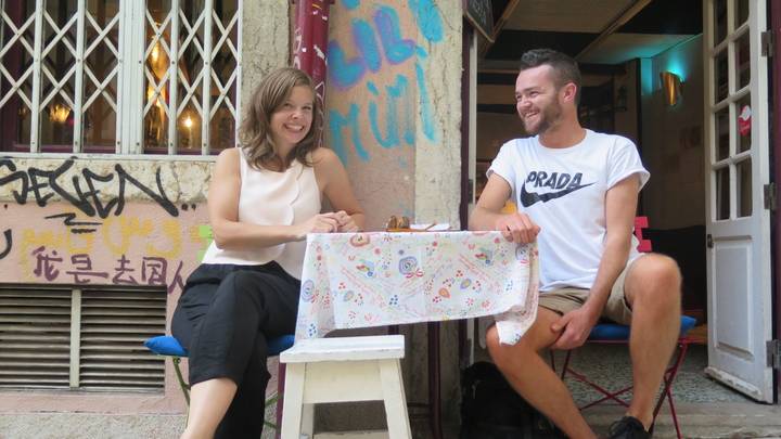 Two people sitting at a small table outside a building with colorful graffiti.