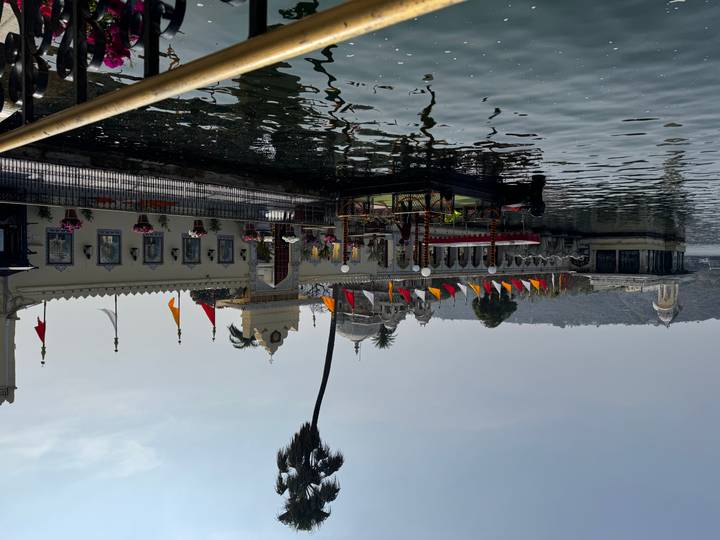 Colourful flags decorate a lakeside palace garden pavilion in Udaipur with reflections on the water.