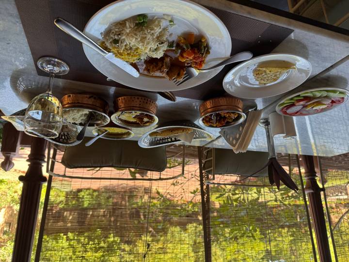 Table set with a spread of Indian curries, rice, salads and wine in a shaded garden restaurant.