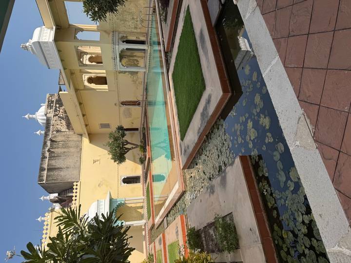 Quiet palace courtyard with rectangular pool, lotus leaves and yellow heritage walls under clear sky.