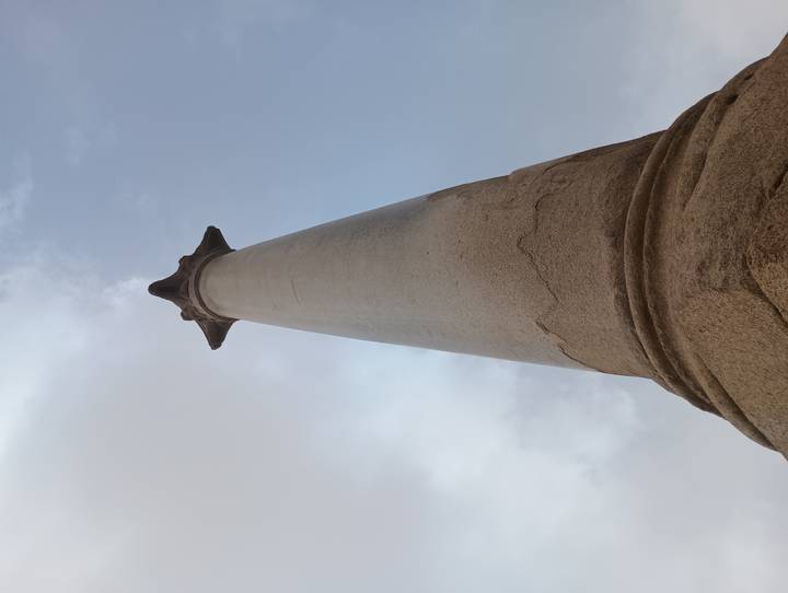 Upward perspective of a towering granite column topped with a star-shaped capital against cloudy sky.