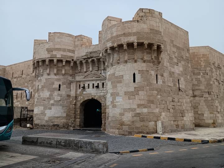 Stone entrance of a medieval coastal fortress with round bastions and arrow slits.