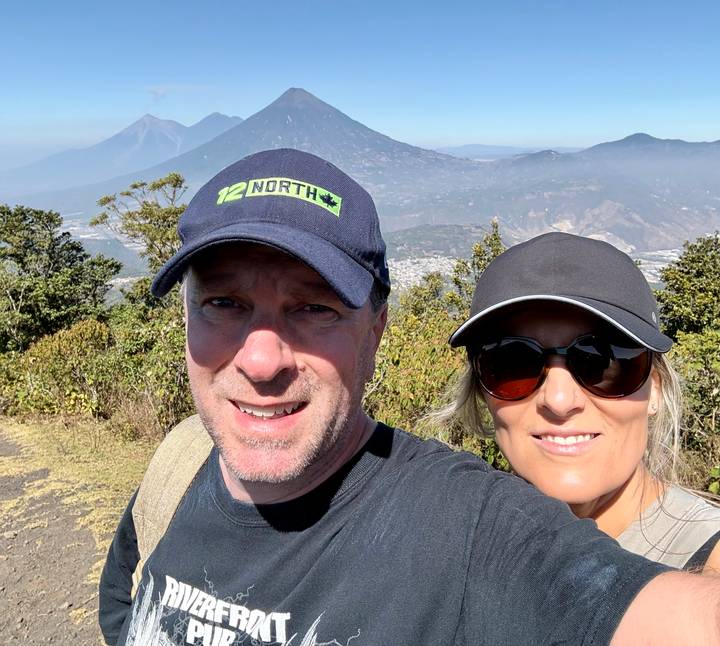 Couple posing on a mountainside trail with a volcanic peak rising behind them