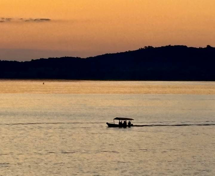 Silhouetted motorboat gliding across a calm lake during a vivid orange sunset
