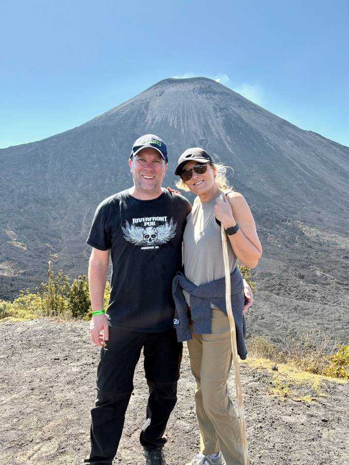 Hikers standing on dark volcanic slope with rocky cone towering above them