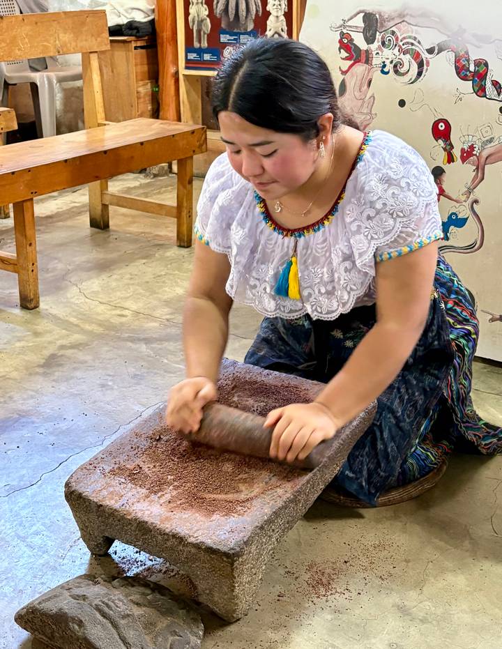 Young girl grinding cacao on a stone slab during a traditional chocolate workshop