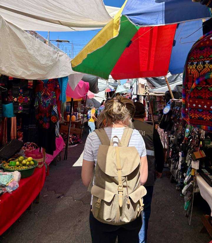Back view of travellers navigating a colourful, crowded market lined with textiles and produce