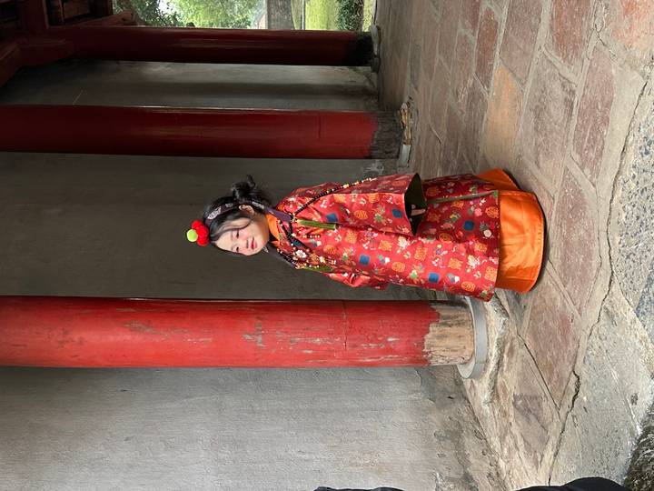 Young girl wearing ornate traditional costume stands by red columns in an ancient courtyard