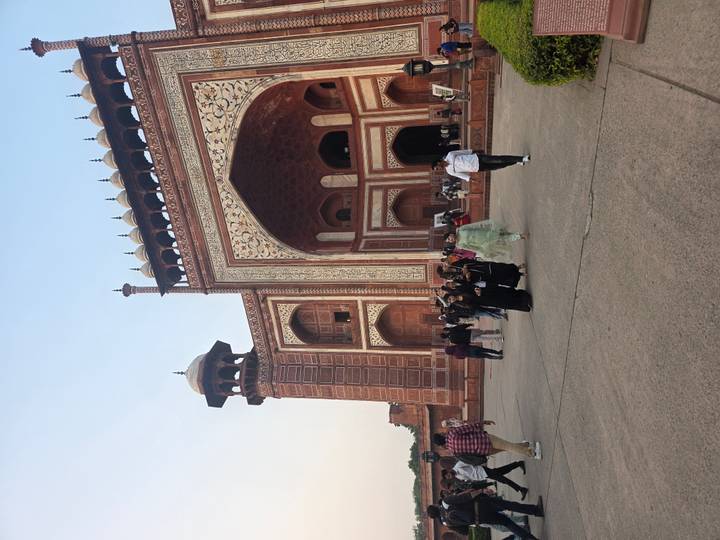 Visitors walking through the grand red sandstone gateway at the entrance to the Taj Mahal complex.