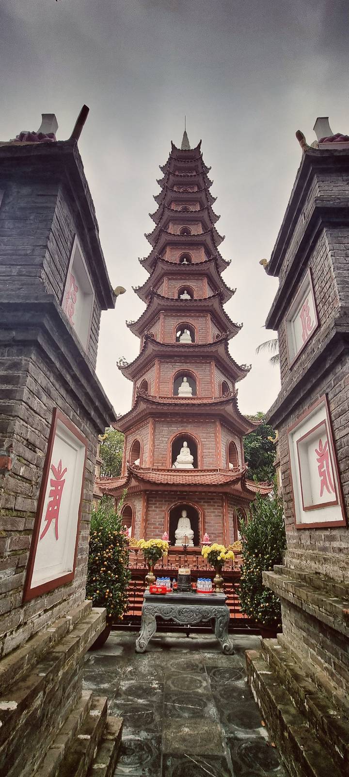 Brick pagoda tower with white Buddha niches framed by aged stone walls on either side.