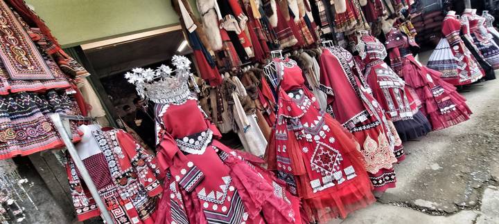 Rows of bright red ethnic dresses and textiles displayed outside a hill-town shop.