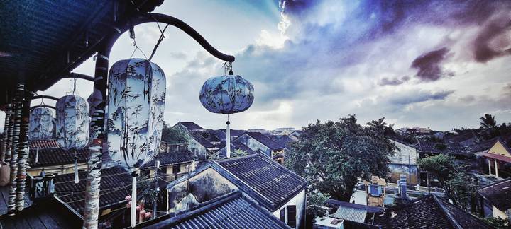 Decorative hanging lanterns silhouetted against dramatic clouds over the rooftops of Hoi An.