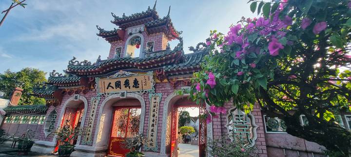 Decorative pink Chinese assembly hall gate in Hoi An with blooming bougainvillea in the foreground.