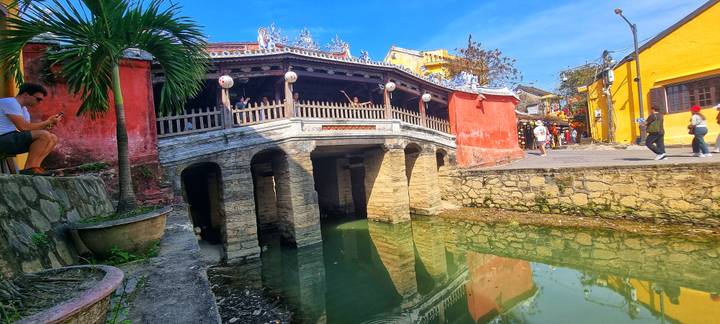 Historic Japanese Covered Bridge crossing a narrow canal in Hoi An’s old town under bright skies.