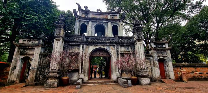 Ancient stone gateway of Hanoi’s Temple of Literature framed by trees and flowering branches.