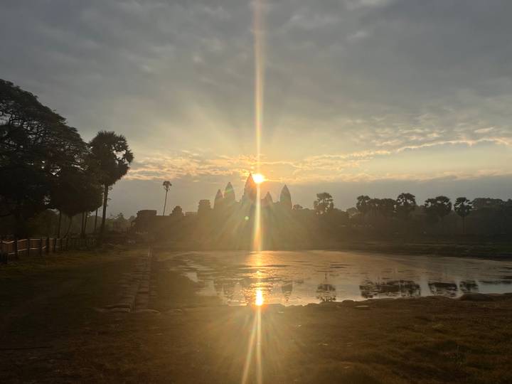 Golden sunrise breaking over the silhouette of Angkor Wat, reflections shimmering in still water