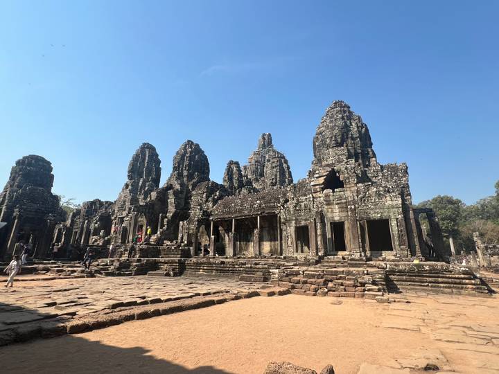 Well-preserved stone faces and towers of Bayon Temple under clear blue sky with scattered visitors