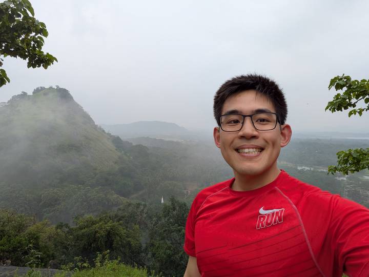 Selfie of a runner with misty forested hill and grey sky in background.