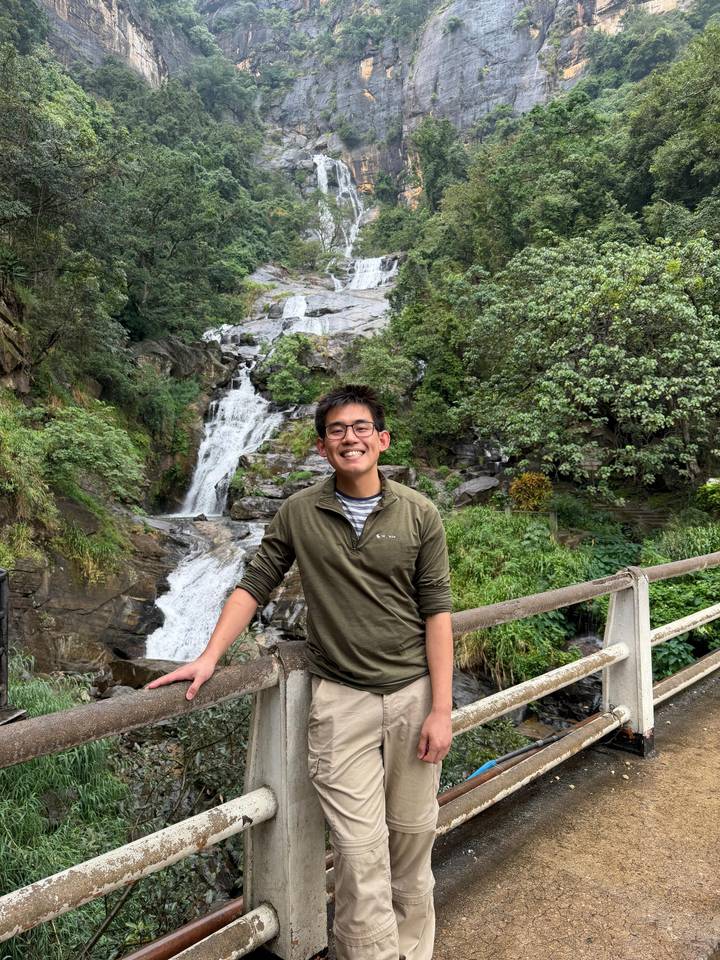 Traveler posing on bridge in front of cascading jungle waterfall.