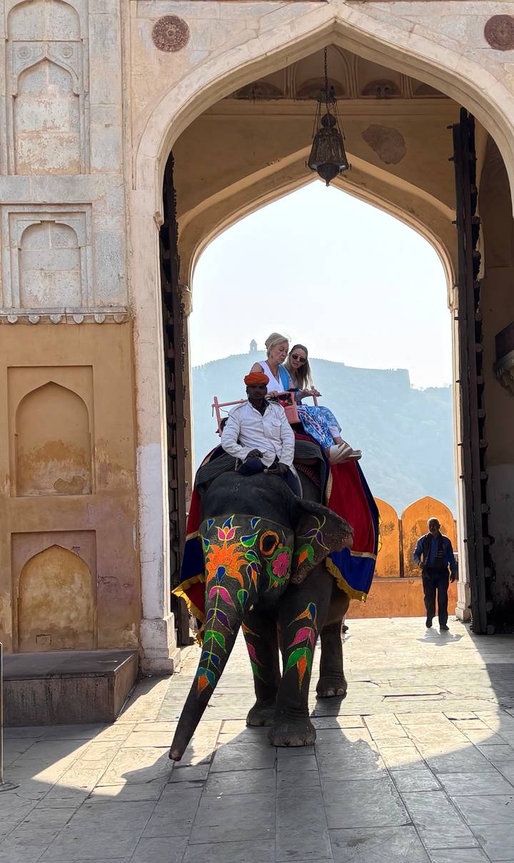 Decorated elephant carrying two tourists passes through a grand fort gateway
