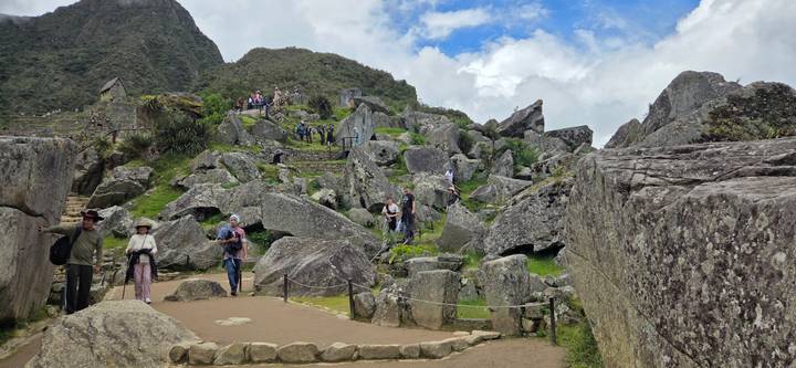 Tourists explore rocky ruins and boulder fields beneath misty Machu Picchu peaks