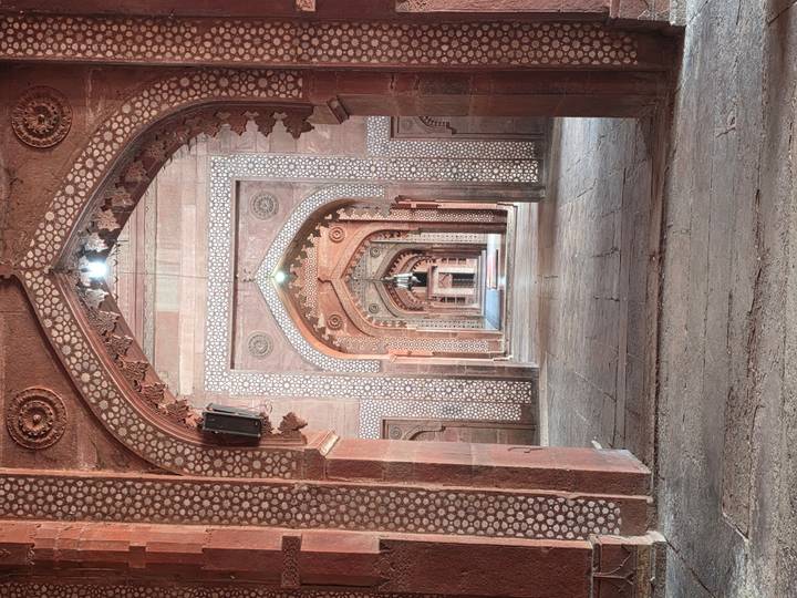 Symmetrical perspective of arched sandstone corridor with intricate inlay patterns at Fatehpur Sikri mosque.