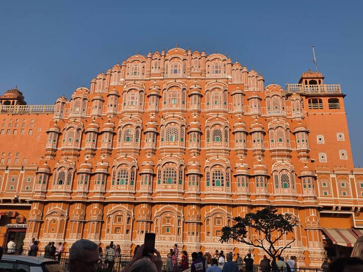 The iconic terracotta façade of Jaipur's Hawa Mahal bathed in bright sunlight against a blue sky.