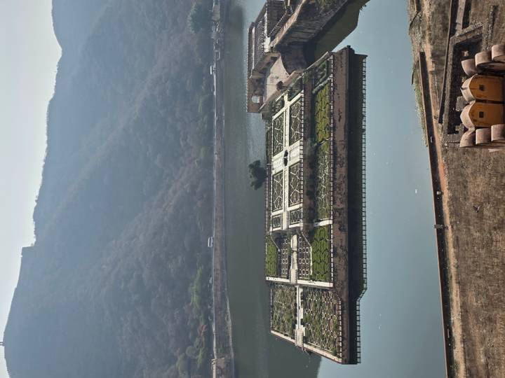 Elevated view of patterned garden islands and a calm lake surrounded by forested hills.