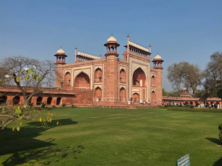 The grand red-sandstone gateway to the Taj Mahal complex framed by manicured lawns under a clear sky.