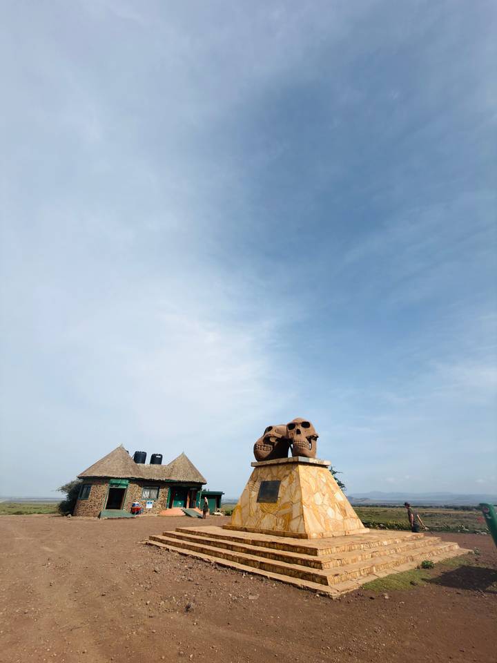 Large sculpted skulls form a roadside monument beneath a vast blue sky.