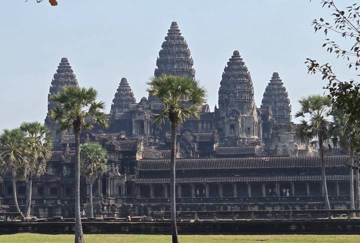 Front view of Angkor Wat's central towers framed by palm trees under a clear sky.