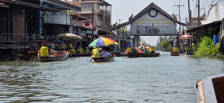 Long-tail boats and vendors navigate a bustling Thai floating market canal.