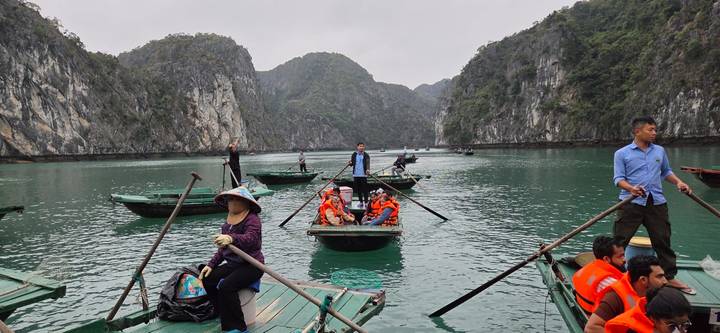 Tourists in rowboats glide through emerald waters flanked by dramatic limestone cliffs.