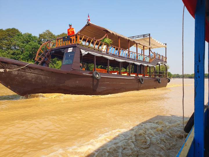 Traditional wooden cruise boat speeds along muddy waters of the Mekong Delta.