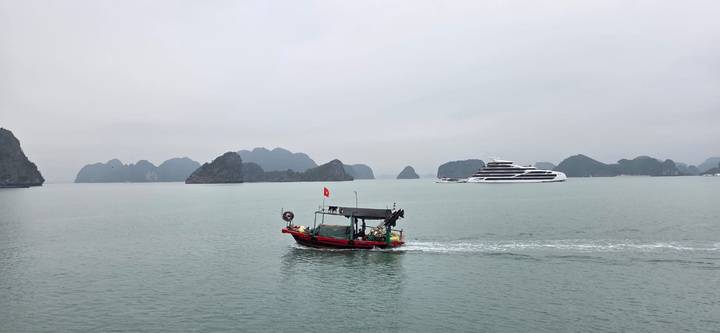 Small fishing boat passes a luxury cruise ship amid misty limestone islands of Halong Bay.