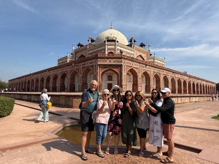 Travel group poses in front of the red-sandstone Humayun’s Tomb under blue Delhi skies.