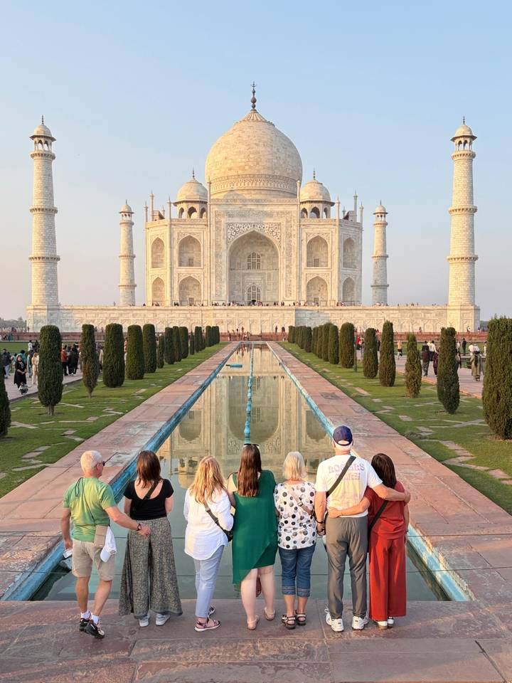 Visitors sit facing the reflecting pool with the majestic Taj Mahal in evening light.