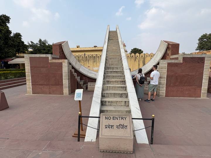 Historic astronomical instrument at Jaipur’s Jantar Mantar with a no-entry sign and tourists nearby.