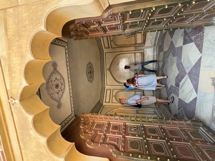 Tourists explore an ornately decorated chamber with patterned walls and mosaic floor.