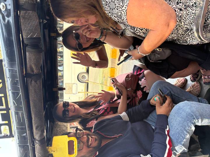 Smiling travelers wave from inside an auto-rickshaw during a city ride.