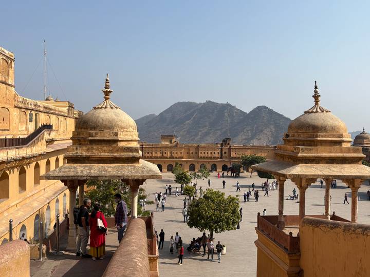 Courtyard of Amber Fort with domed pavilions overlooks hills under bright blue sky.