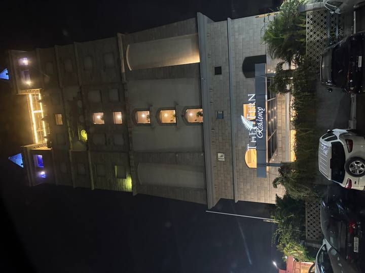 Tall modern hotel building lit at night with cars parked in front.