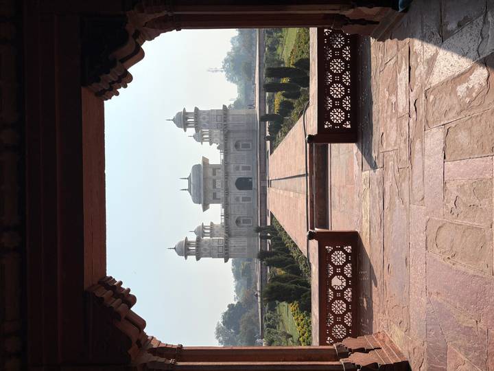 Symmetrical view of the sandstone and marble Itimad-ud-Daulah tomb framed by an arched doorway.