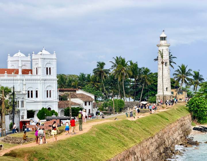 Crowds explore Galle Fort’s white lighthouse and colonial buildings framed by tropical palms