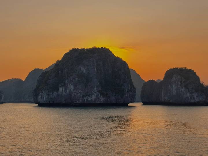 Golden-hour view of karst islands rising from calm water in Ha Long Bay at sunset.