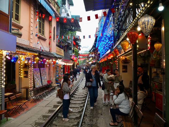 Vibrant Hanoi Train Street with cafés, lanterns, and tourists walking along the railway track.