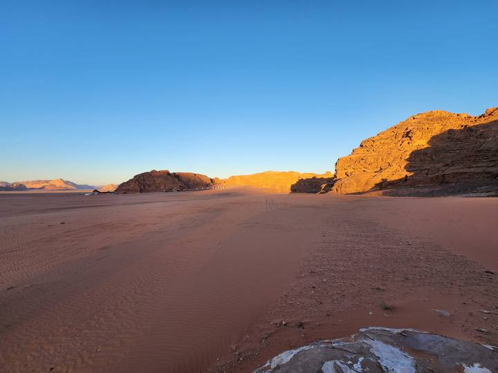 Vast empty desert valley with red-tinted cliffs glowing in low evening light under clear blue sky